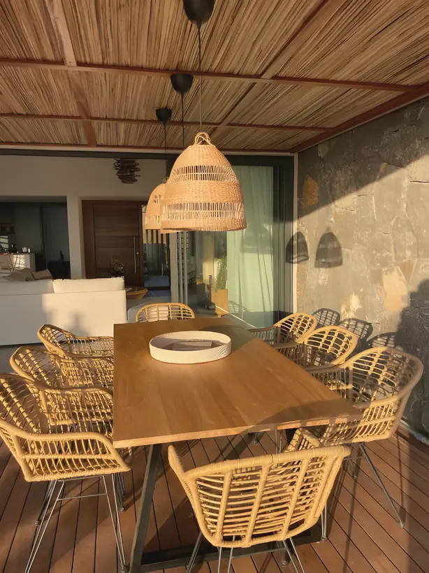 Outdoor dining table with rattan chairs under a woven pendant